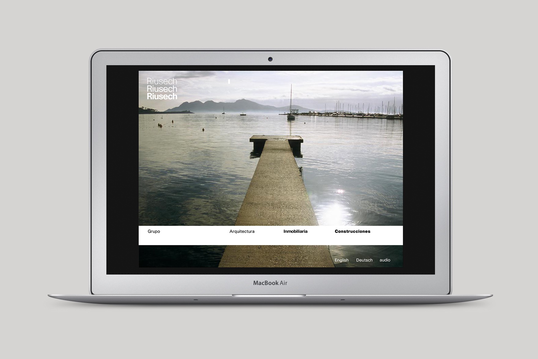 Macbook Air mockup of a landing page design for RIUSECH GROUP. Includes a port background, header contains &ldquo;arquitectura, inmobiliaria, construcciones &rdquo;. Website designed by Esiete branding and communication studio and programmed by sevenap.net