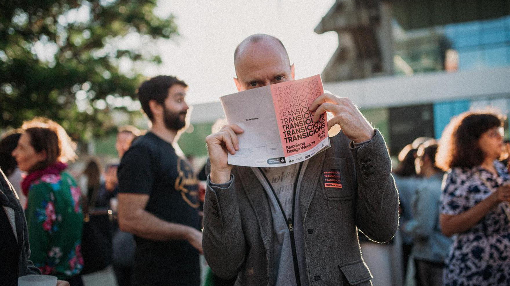<span><span>Home a l'exterior de l'esdeveniment DESIGN WEEK 2019, amb el flayer de l'esdeveniment a la cara. Dissenyat per l'estudi </span><span>esiete</span><span> de branding i comunicaci&oacute;.</span></span>