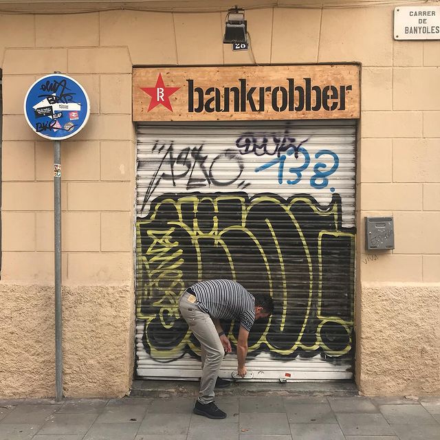 <span><span>A man opens the front door of Bankrobber. The shop facade has the logo design of Bankrobber that was designed by Esiete branding and communication studio/agency Barcelona Spain.</span></span>