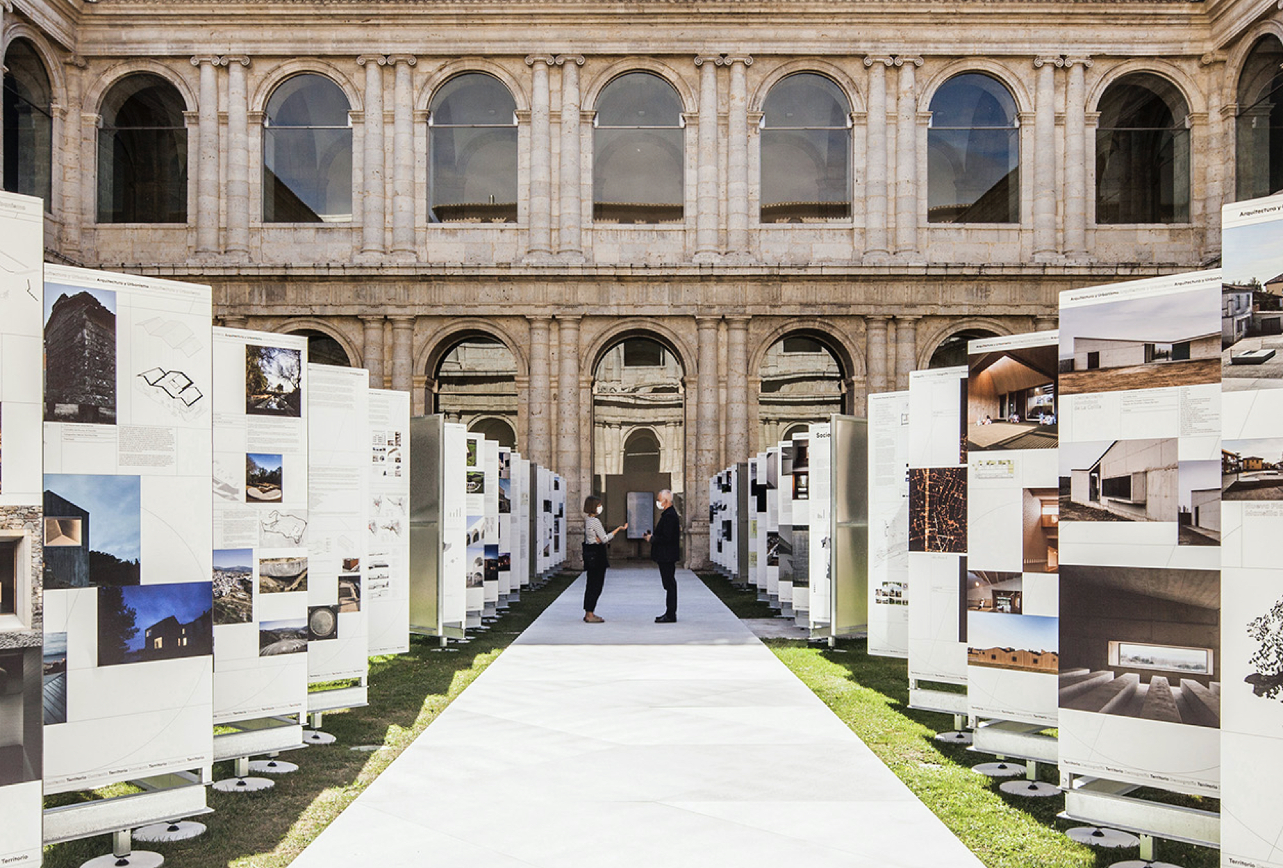 <span><span>Imatge de l'exposici&oacute; XV Biennal Espanyola d'Arquitectura i Urbanisme on apareixen dues persones interactuant enmig de dues s&egrave;ries de cartells en forma de ziga-zaga. Dissenyat per l'estudi esiete de branding i comunicaci&oacute;.</span></span>