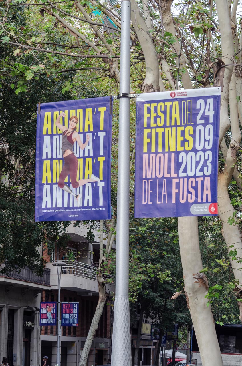 <span><span>Fotografia d'un cartell en un fanal dels carrers de Barcelona per a la campanya de LA FESTA DEL FITNES 2023. Amb el missatge de ANIMA&rsquo;T i una fotografia d'una noia feli&ccedil;, saltant i vestida amb roba d'esport. Dissenyat per l'estudi esiete de branding i comunicaci&oacute;.</span></span>