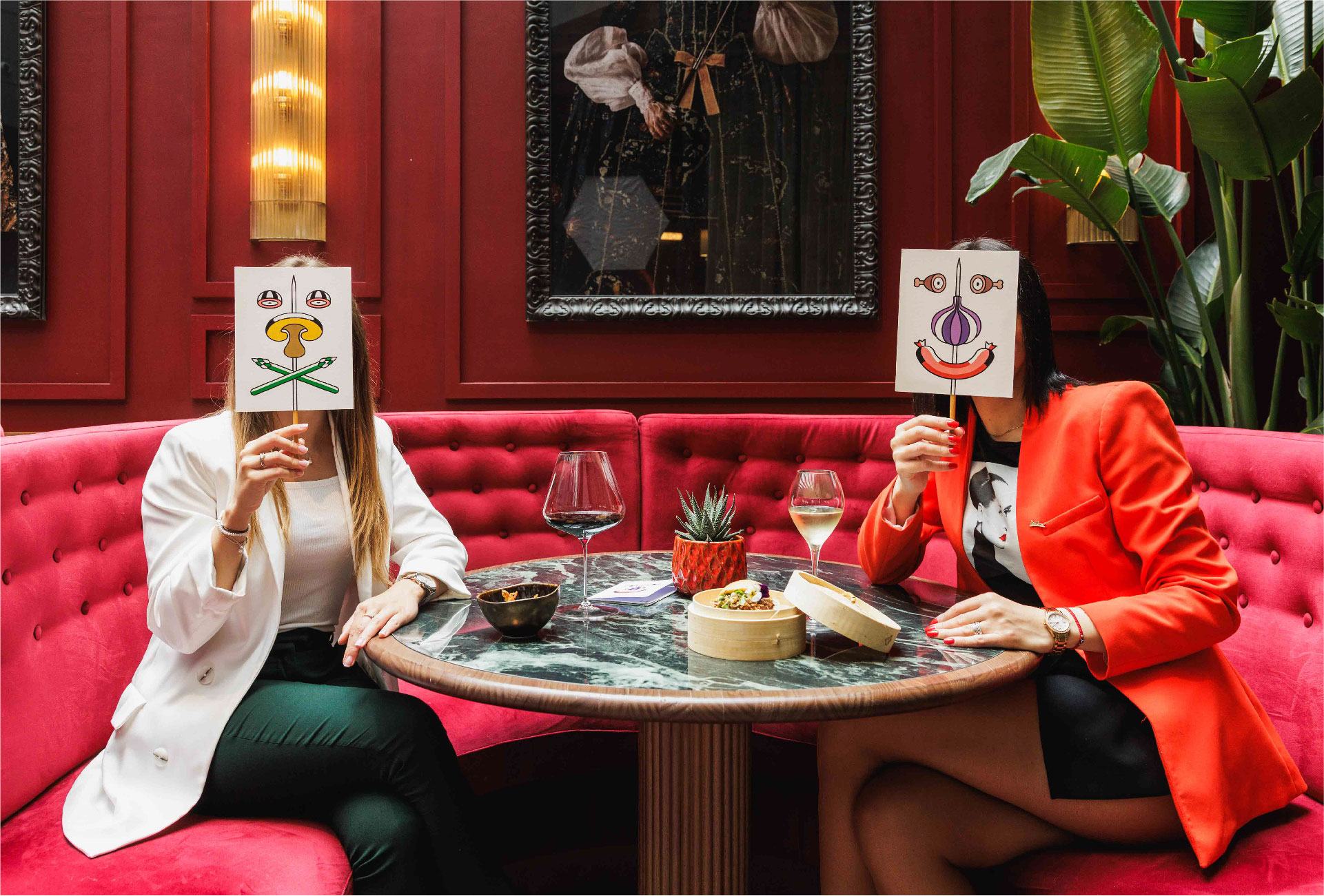 <span><span>Fotograf&iacute;a de dos chicas sentadas en una mesa con dos copas de vino y diferentes tapas, las cuales se est&aacute;n tapando la cara con un cartel con un elemento de la gr&aacute;fica de HOTEL TAPA TOUR 2023, la cual forma una cara. Dise&ntilde;ado por el estudio esiete de branding y comunicaci&oacute;n.</span></span>