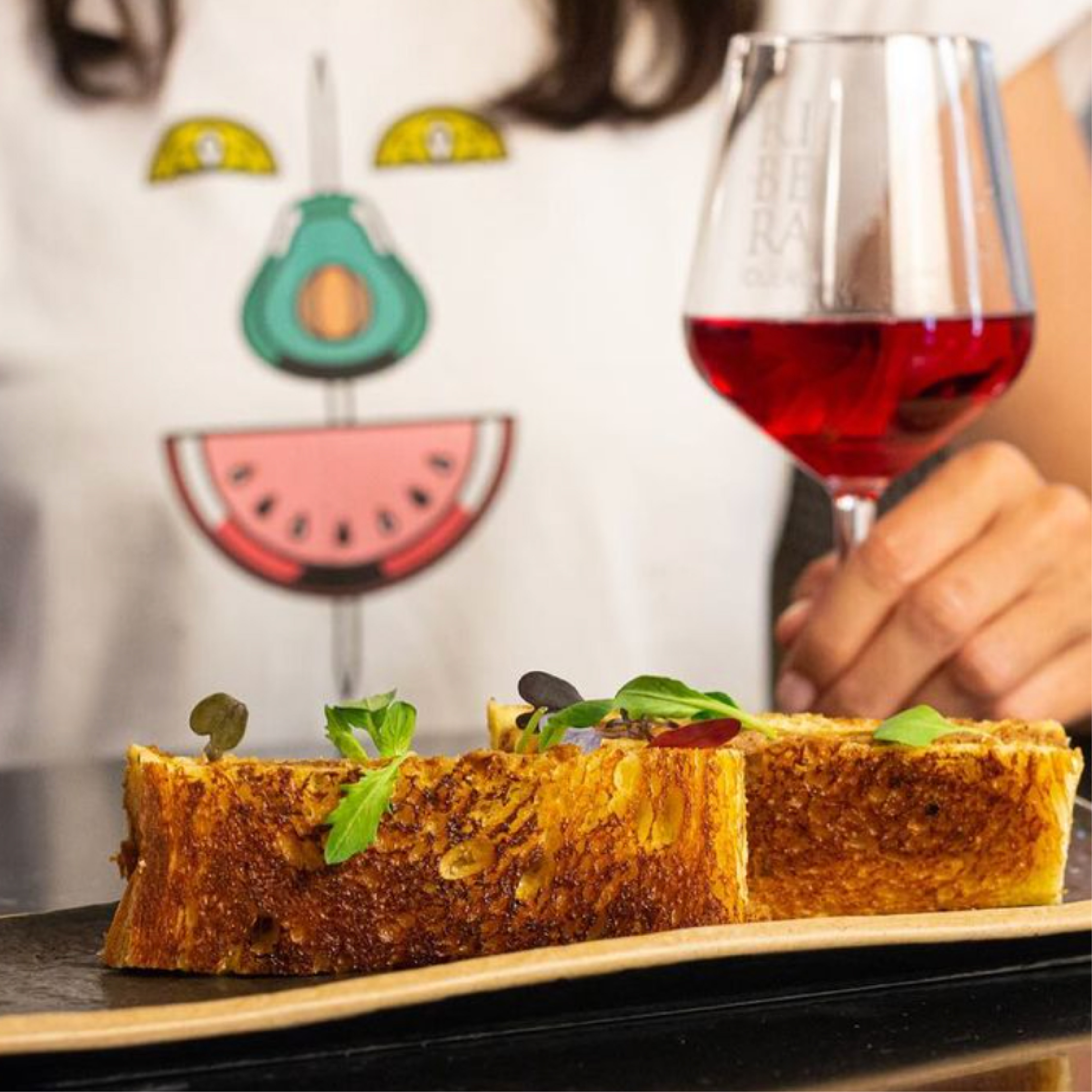 <span><span>Fotograf&iacute;a de una chica tomando vino y una tostada de pan, con una camiseta con el elemento de la gr&aacute;fica de HOTEL TAPA TOUR 2023. Dise&ntilde;ado por el estudio esiete de branding y comunicaci&oacute;n.</span></span>